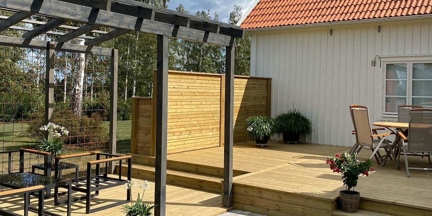 Altan med mörk målad pergola, sittgrupp och trappsteg i trädäck, byggd av Tommy Axelssons Byggservice
